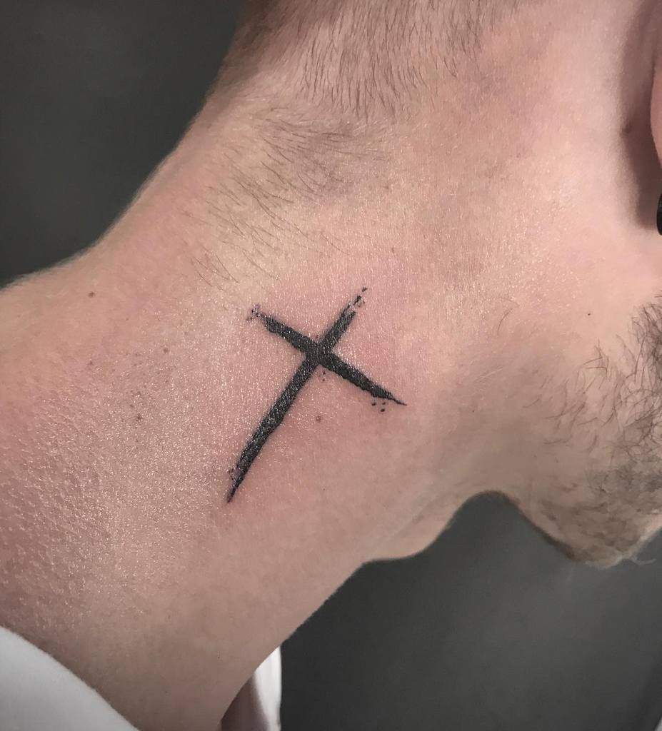 A small black cross tattooed on the side of a man's neck