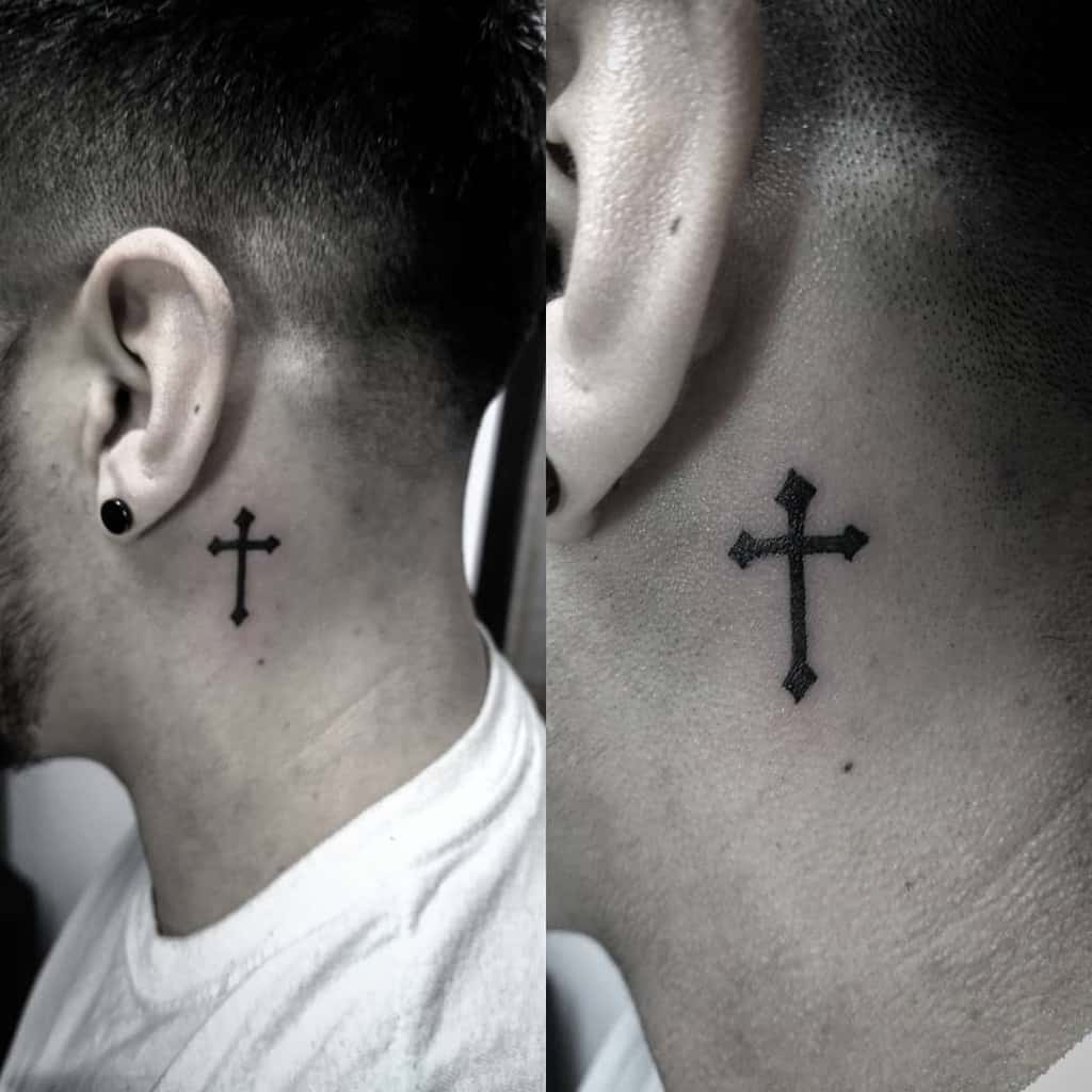 Minimalistic black cross tattoo behind the ear, combining a subtle yet impactful religious and modern design