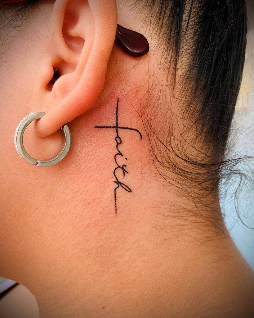 Elegant cross tattoo behind the ear with 'faith' integrated into the design, symbolizing hope and spirituality