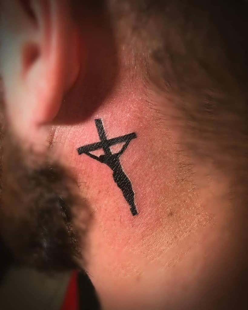Bold black crucifix tattoo behind the ear, featuring a minimalist yet impactful representation of faith