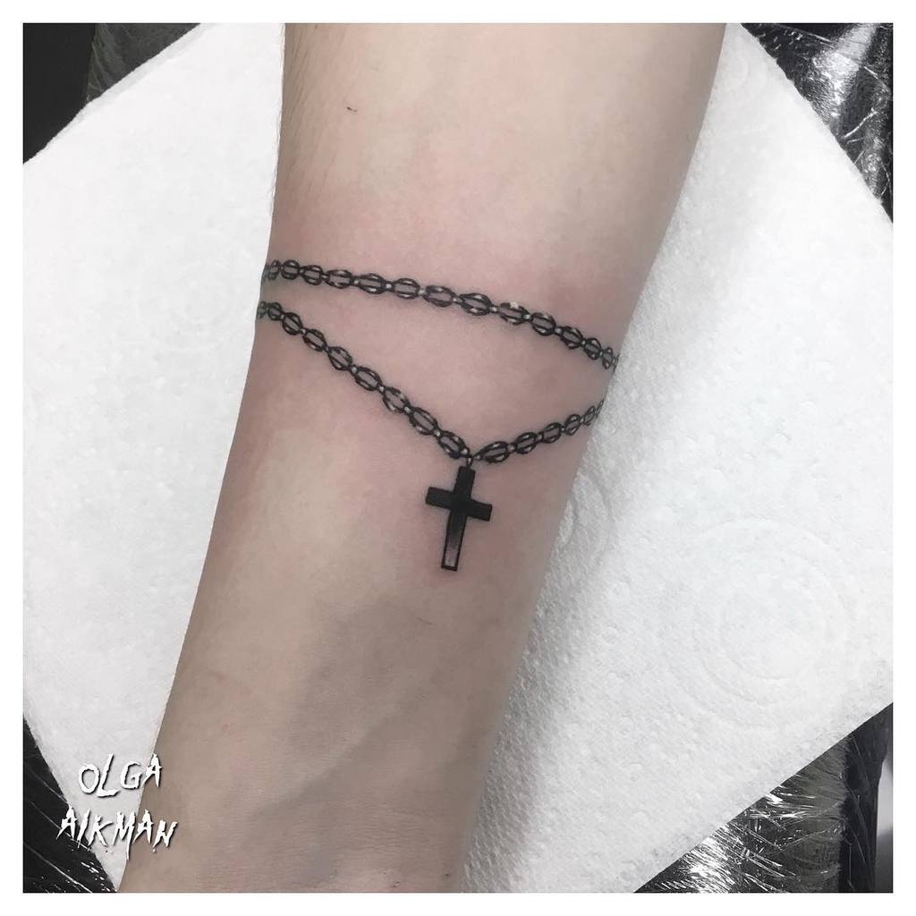 Tattoo of a black rosary with a cross wrapped around a forearm
