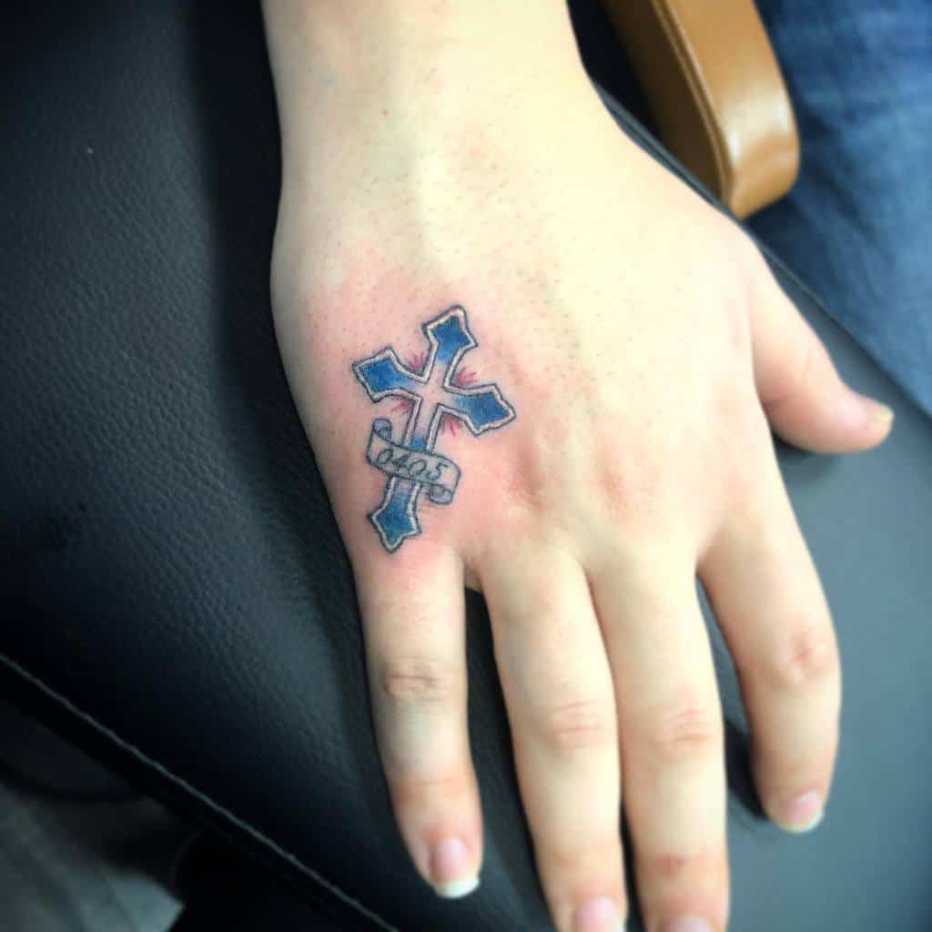 Hand with a tattoo of a stylized cross and banner on the back