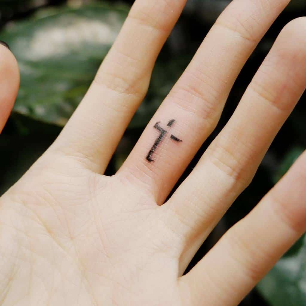 A simple black cross tattoo on a  finger