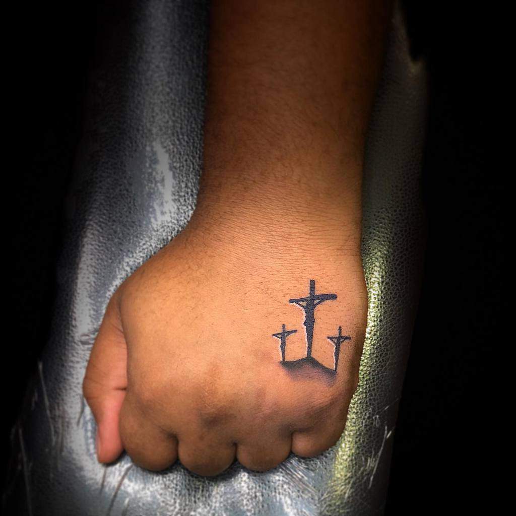 Three crosses tattoo on the hand, symbolizing faith and the crucifixion, with bold and meaningful detailing