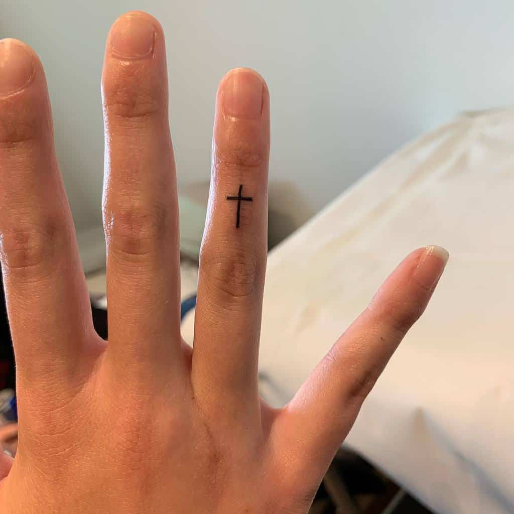 Hand showing a small cross tattoo on the inside of the ring finger