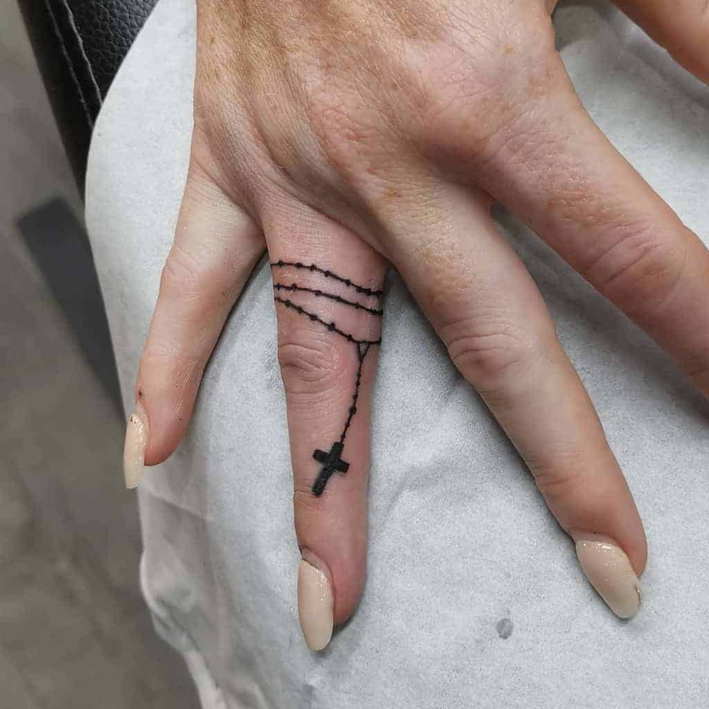 Hand with a rosary tattoo on the finger, featuring a cross and beads