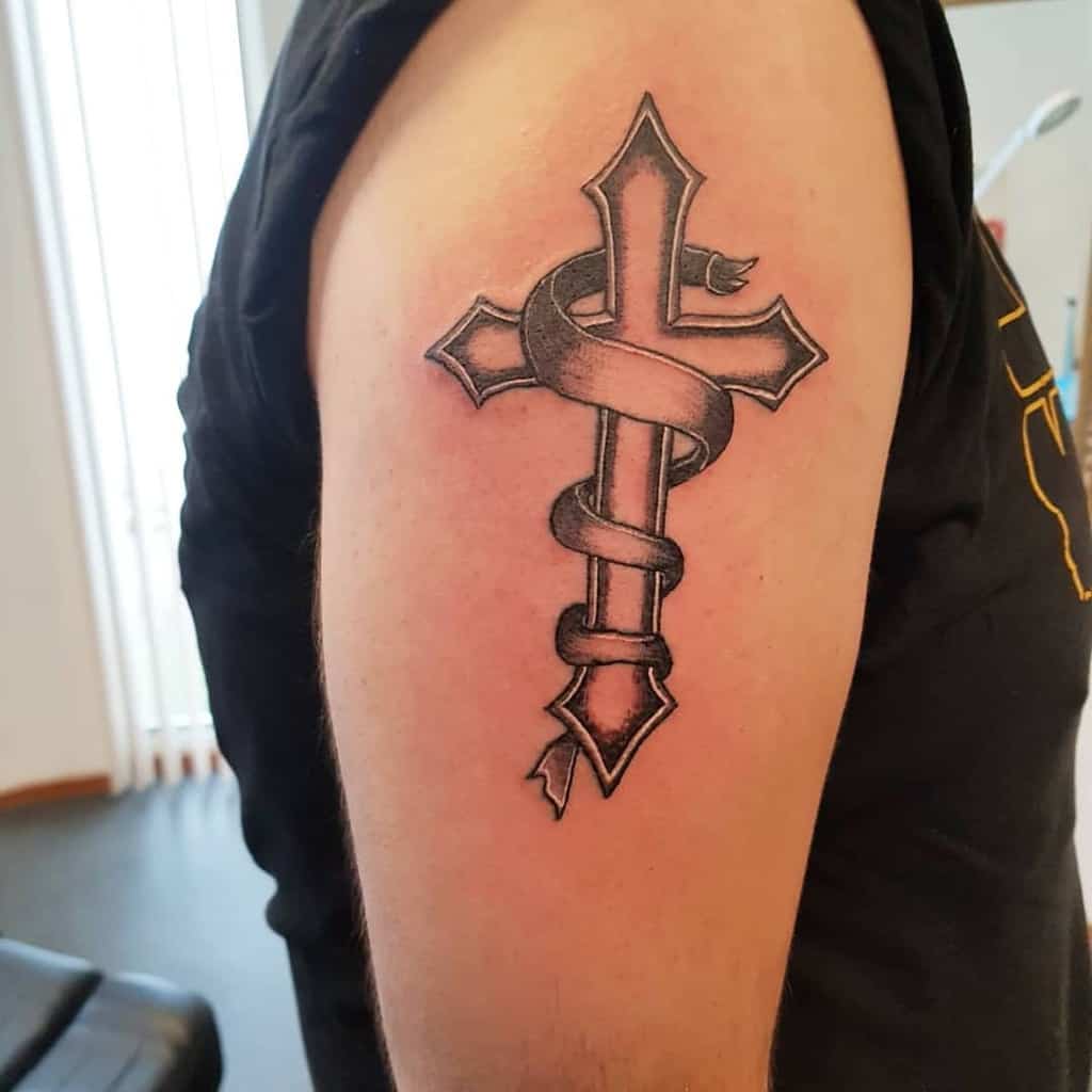 Tattoo of a cross with a ribbon wrapped around it on an upper arm