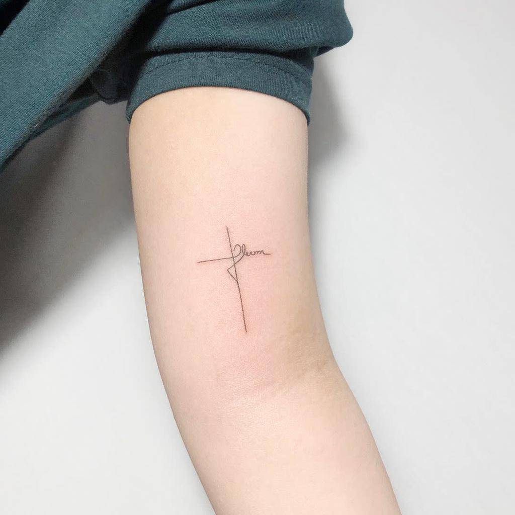 Minimalist cross tattoo with the word "faith" on an arm