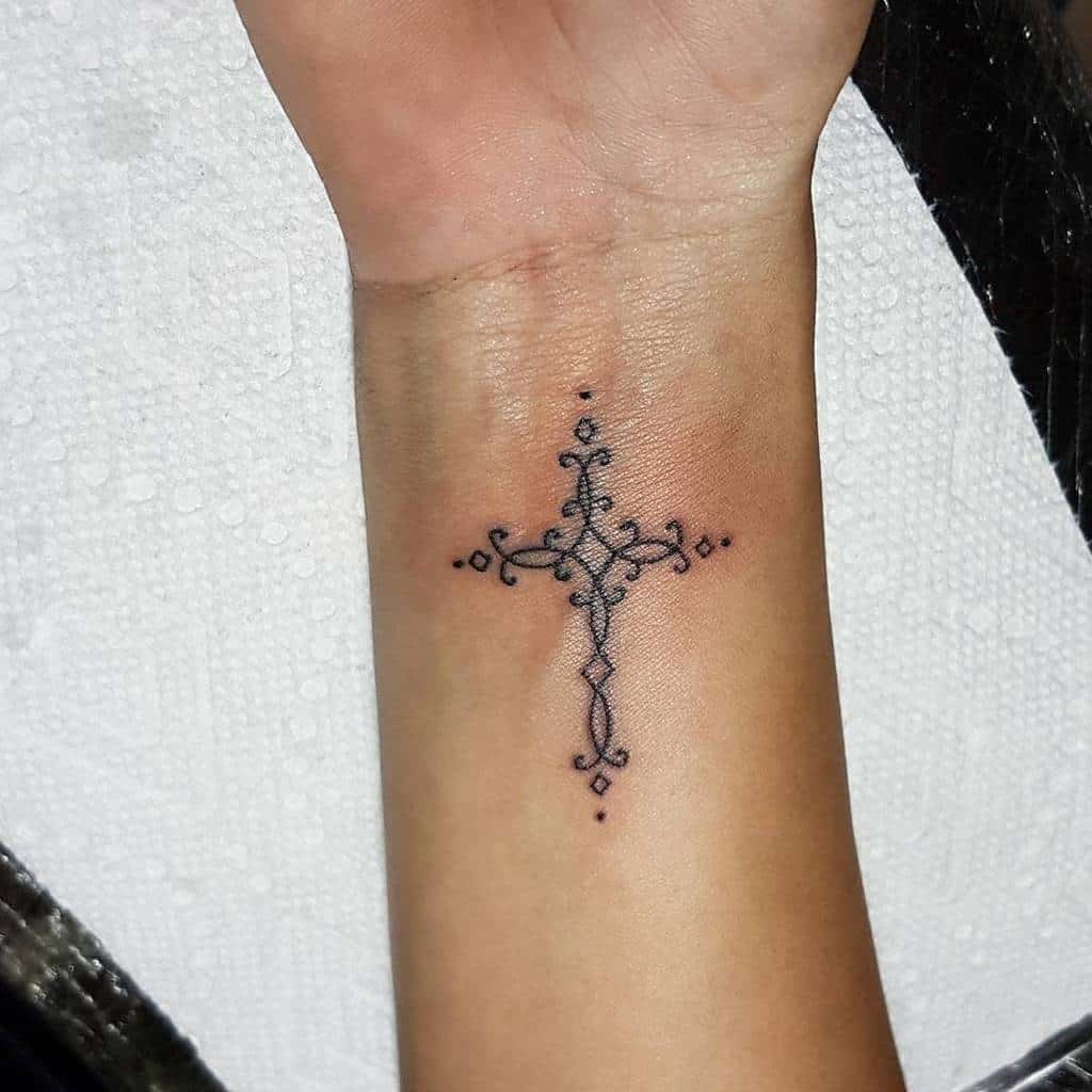 Ornate cross tattoo on a wrist with dotted accents