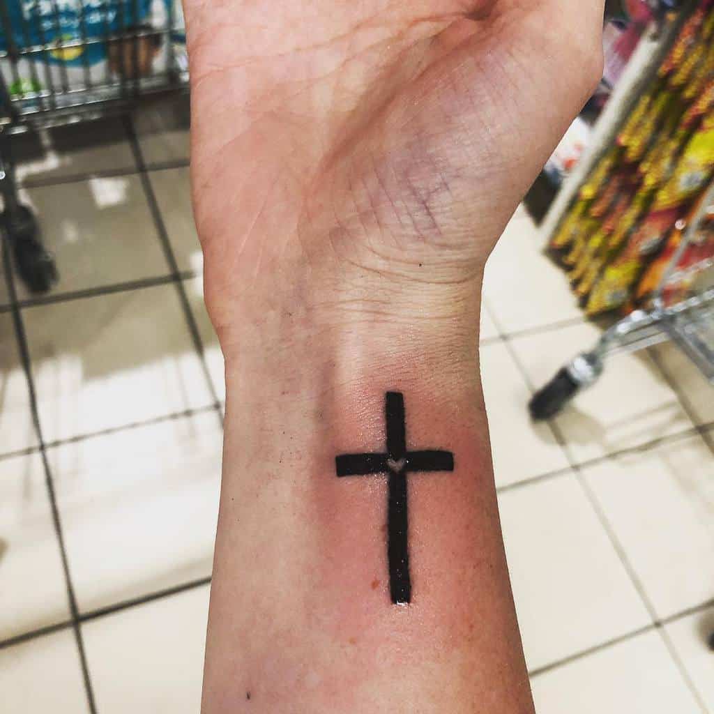 A black cross tattoo on a person's inner wrist