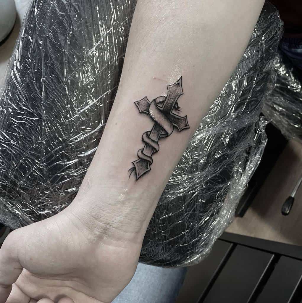 Wrist tattoo of a cross with a snake wrapped around it