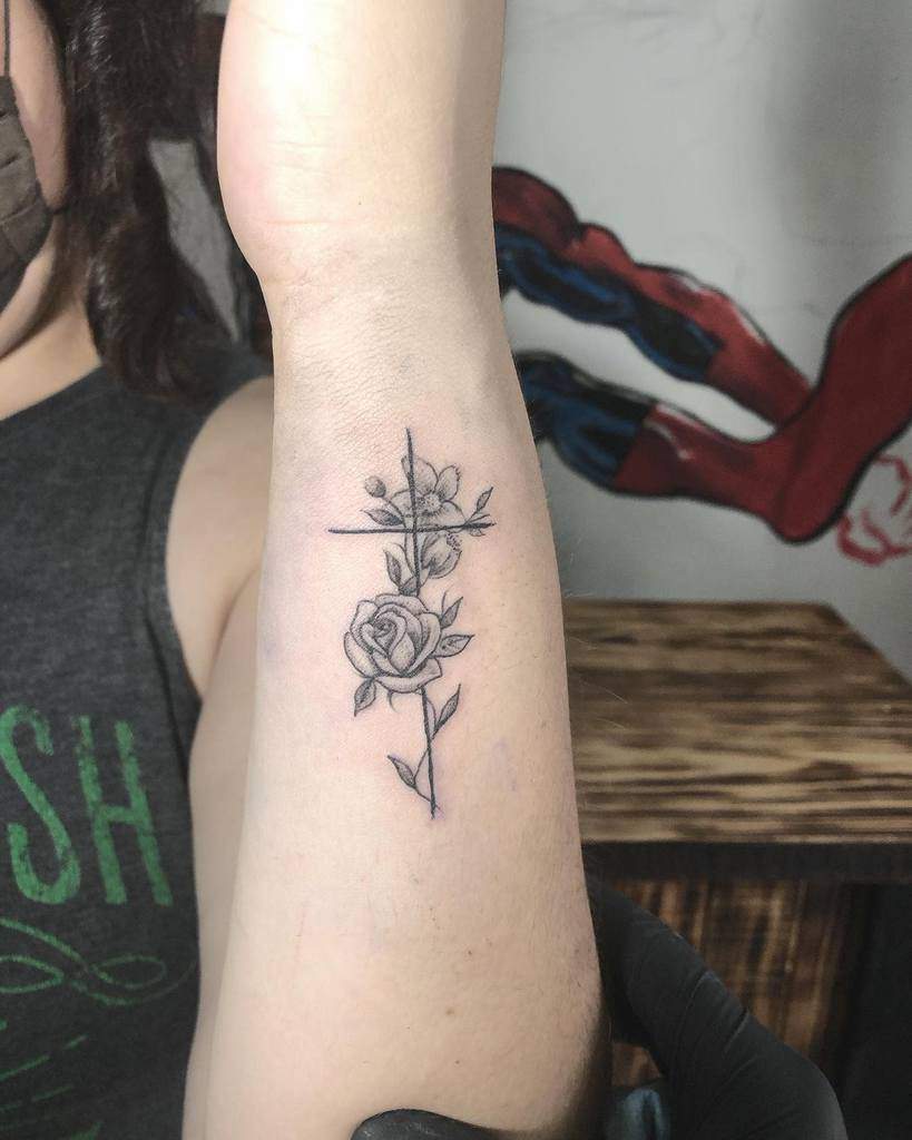 Arm tattoo of a cross intertwined with a blooming rose and leaves