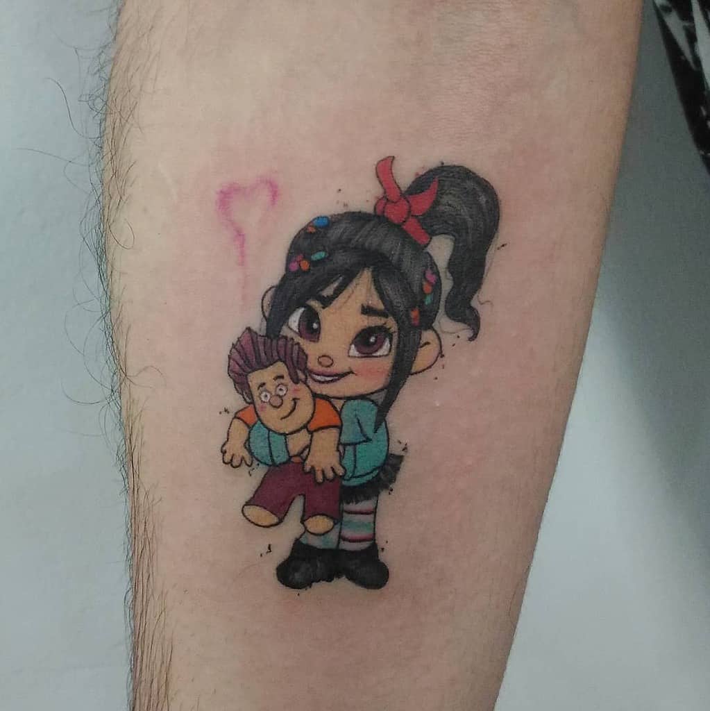 A vibrant tattoo of Vanellope von Schweetz from Wreck-It Ralph, playfully holding her friend, with bright colors and a cute, cartoonish style on the arm