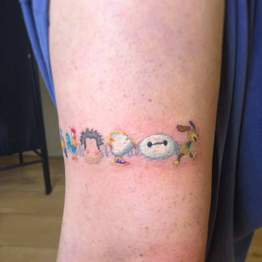 A colorful tattoo featuring a line-up of various Disney characters, including Stitch, a rooster, a hedgehog, and Baymax, creatively placed on the arm