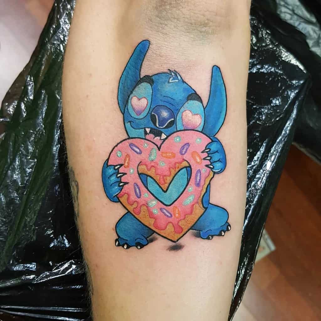 A playful tattoo of Stitch from Lilo& Stitch holding a colorful donut shaped like a heart, designed with vibrant colors and a cute expression