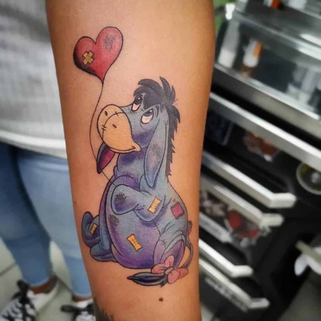 A heartwarming tattoo of Eeyore from Winnie the Pooh, patched up with band-aids, holding a red heart-shaped balloon, designed with soft colors and a gentle expression