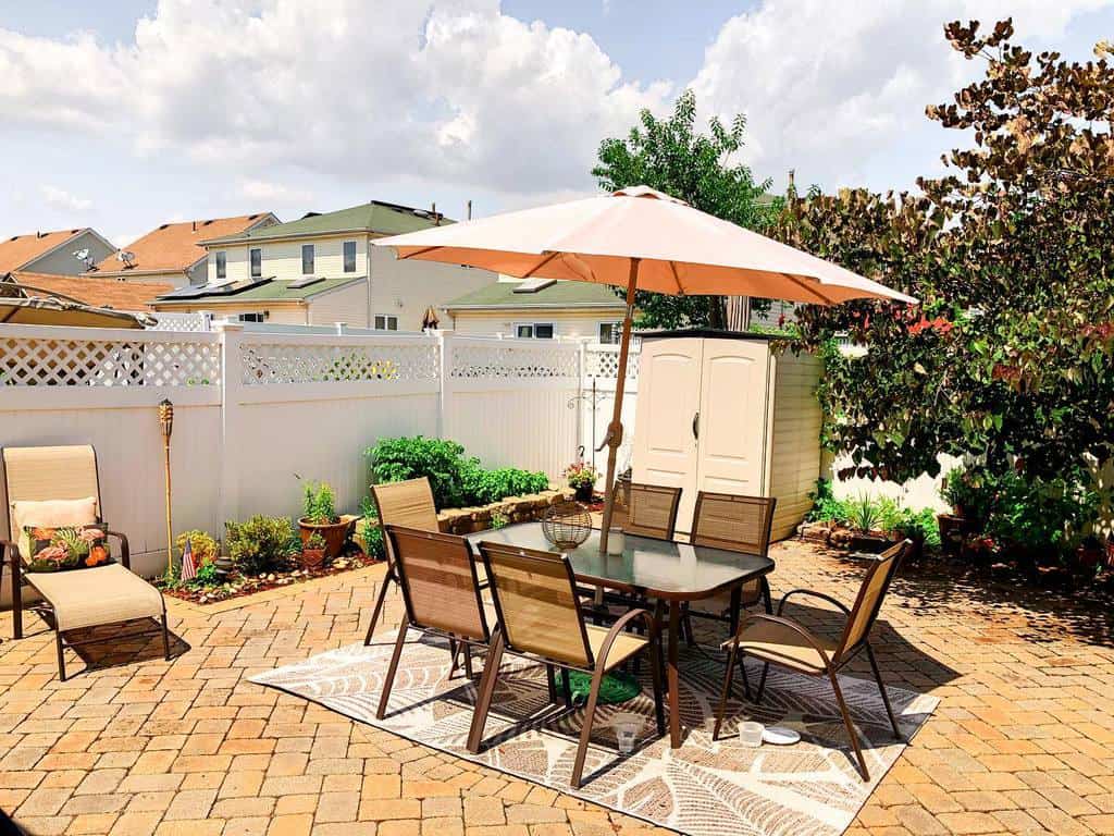 paved patio glass tabletop brown chairs umbrella small garden shed