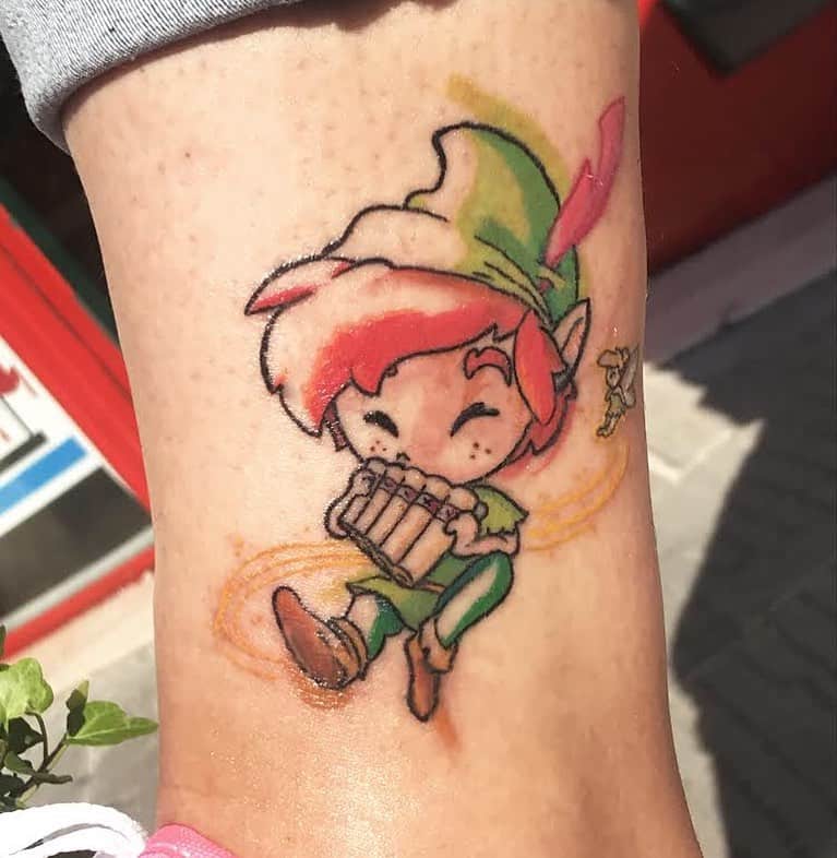 A colorful tattoo of Peter Pan playing the pan flute, with a playful and whimsical design on the ankle