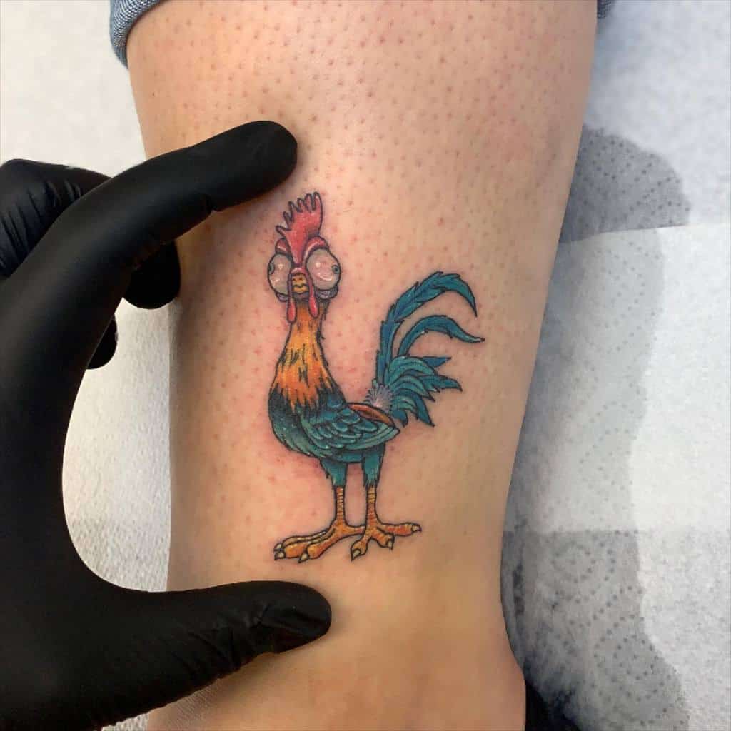 A vibrant and colorful tattoo of a rooster with exaggerated features, playfully standing on an ankle, showcasing a unique and animated style