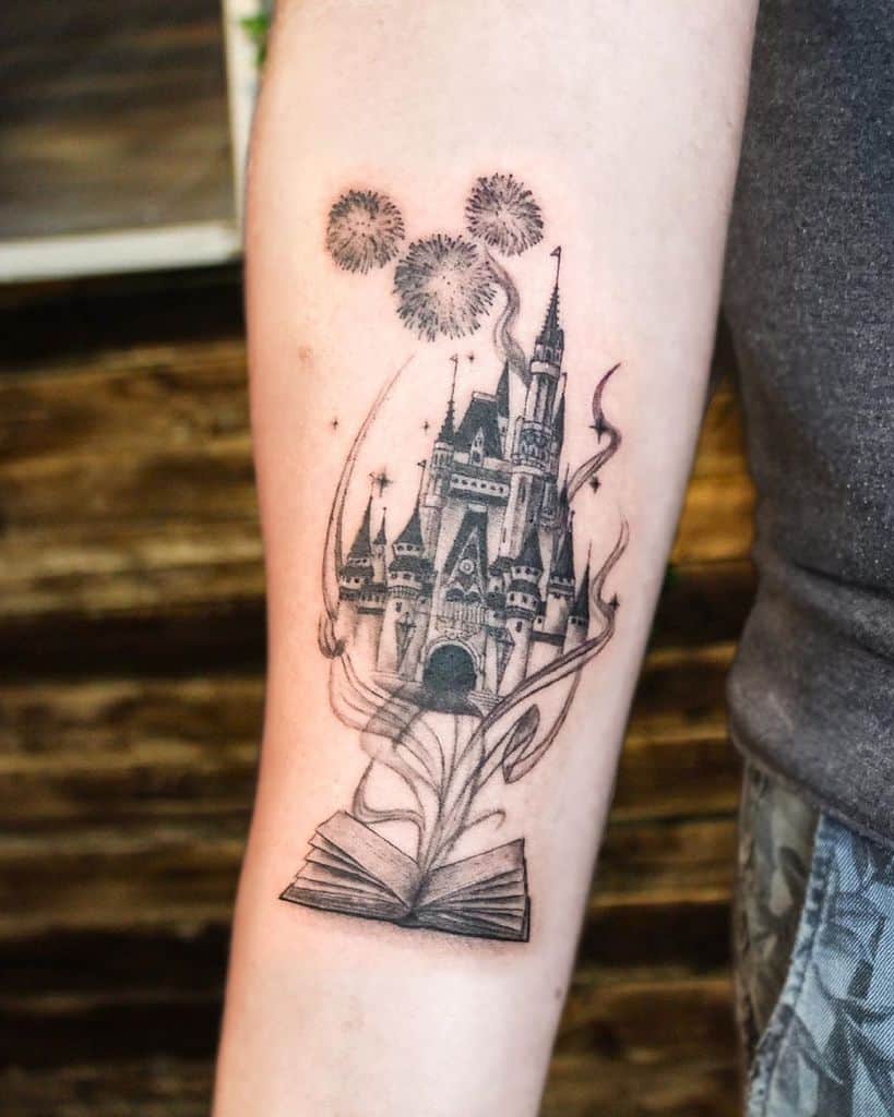 A black and grey tattoo of a Disney castle surrounded by whimsical swirls and fireworks, elegantly placed on the forearm