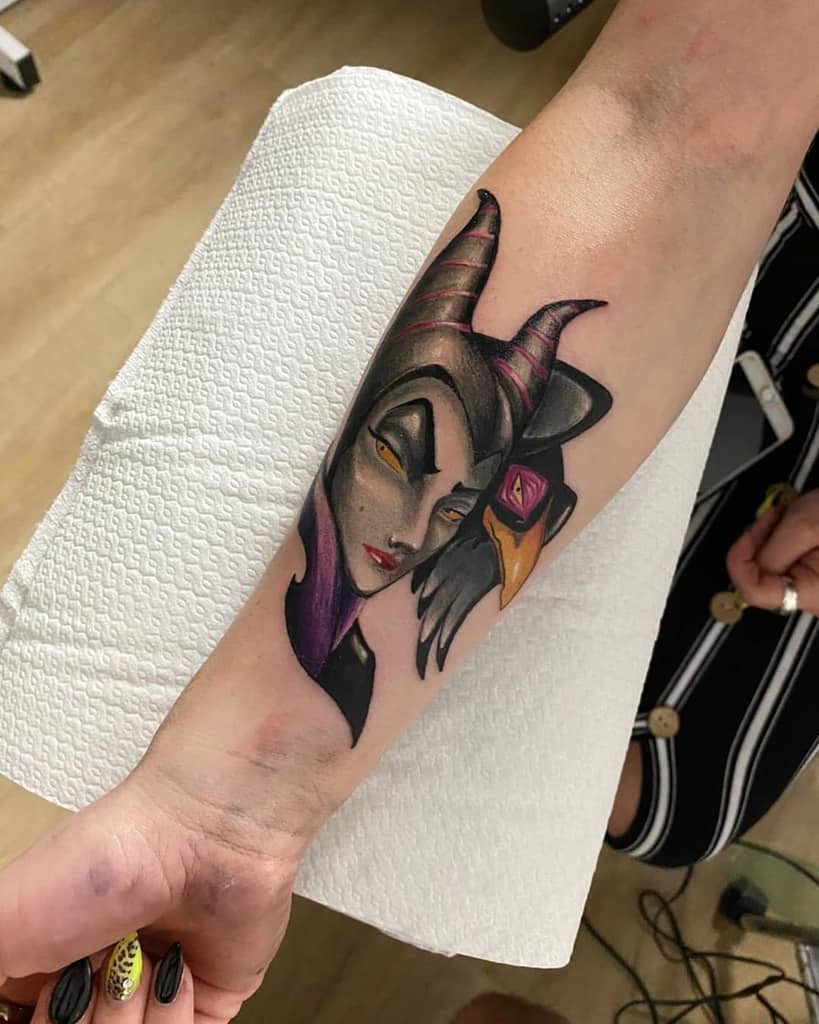 A stunning tattoo of Maleficent, portrayed with intricate details, showcasing her iconic horns and a raven perched on her shoulder, beautifully designed on the forearm