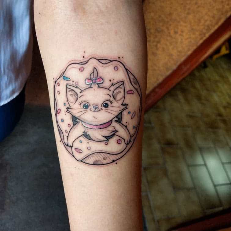 A cute tattoo of Marie from The Aristocats, playfully sitting inside a donut with colorful sprinkles, designed in a soft, pastel color palette on the forearm