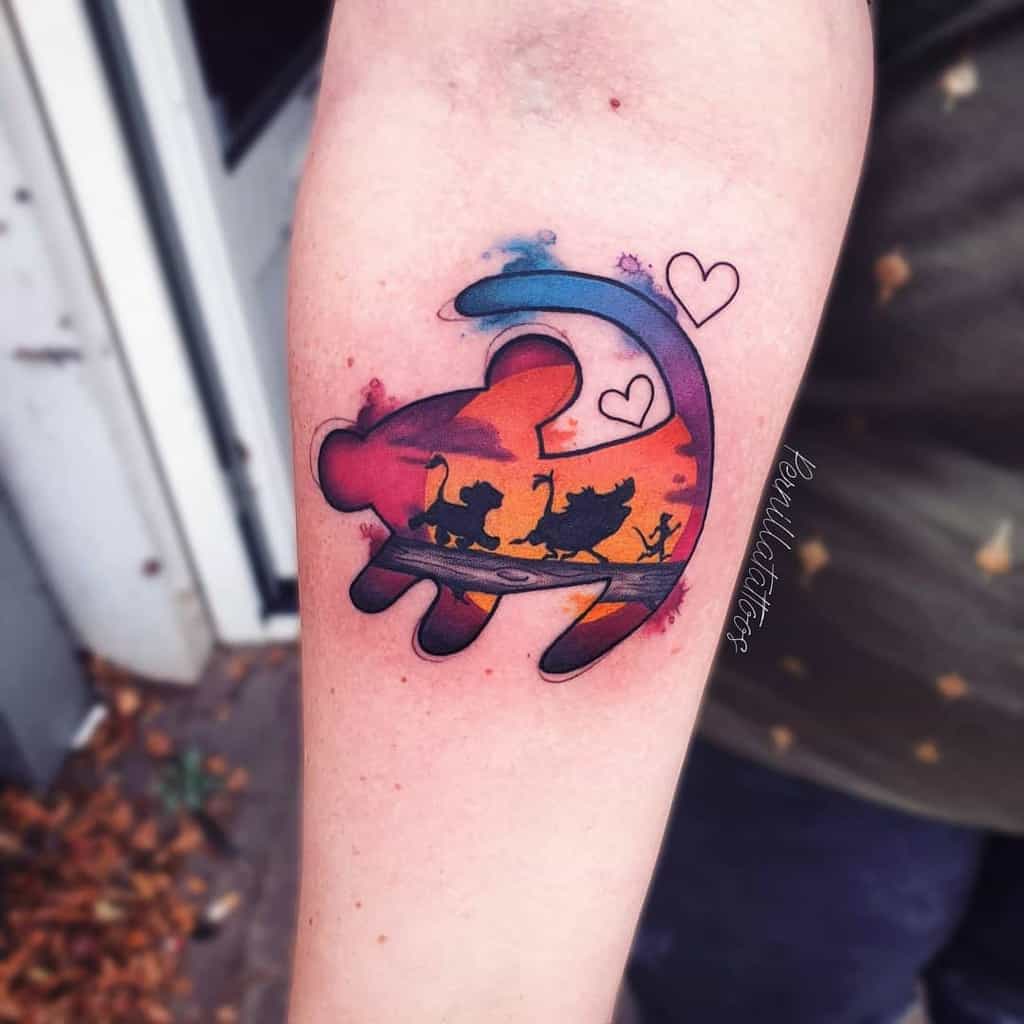 A colorful Lion King tattoo with a Simba silhouette and sunset, framed by hearts, capturing a nostalgic moment