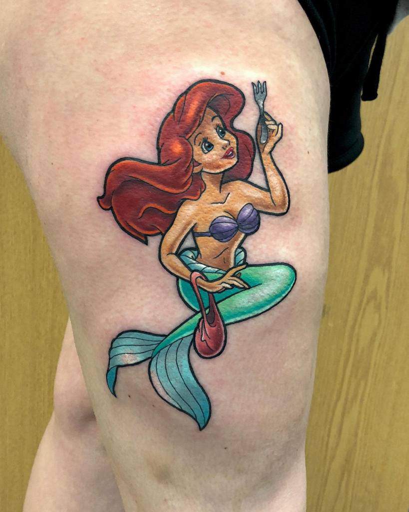 A vibrant tattoo of Ariel from "The Little Mermaid" holding a fork, also known as a "dinglehopper," symbolizing her curiosity about human objects
