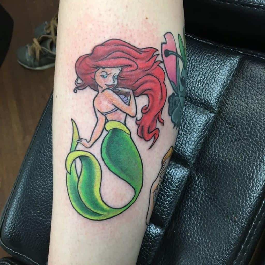 A colorful tattoo of Ariel from "The Little Mermaid," showing her gracefully positioned with her signature flowing red hair and green tail