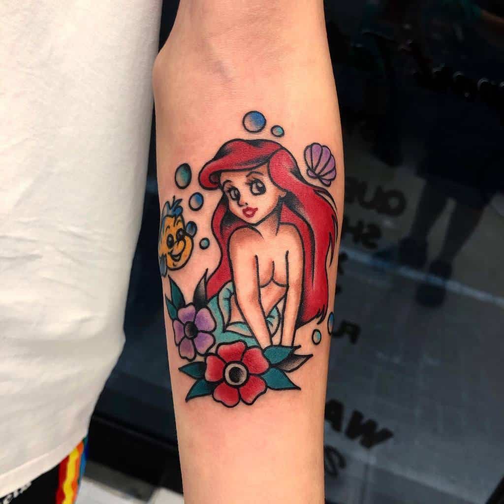 A vibrant tattoo of Ariel from "The Little Mermaid," featuring her surrounded by bubbles, colorful flowers, and her companion Flounder