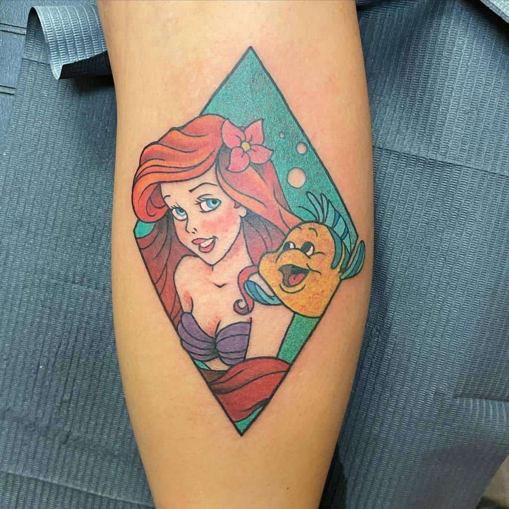 A vibrant tattoo featuring Ariel and Flounder inside a diamond-shaped frame, showcasing their close friendship and playful bond