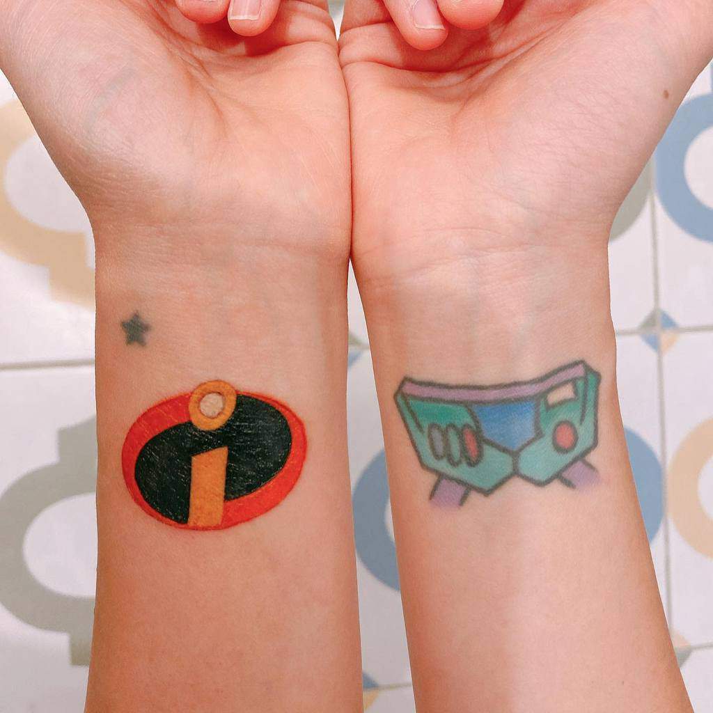 Two forearm tattoos: one with The Incredibles logo, the other a stylized toaster