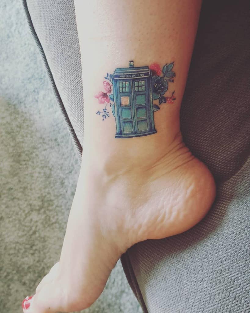 Charming tattoo featuring the TARDIS from 'Doctor Who', surrounded by a cluster of delicate blue and pink flowers