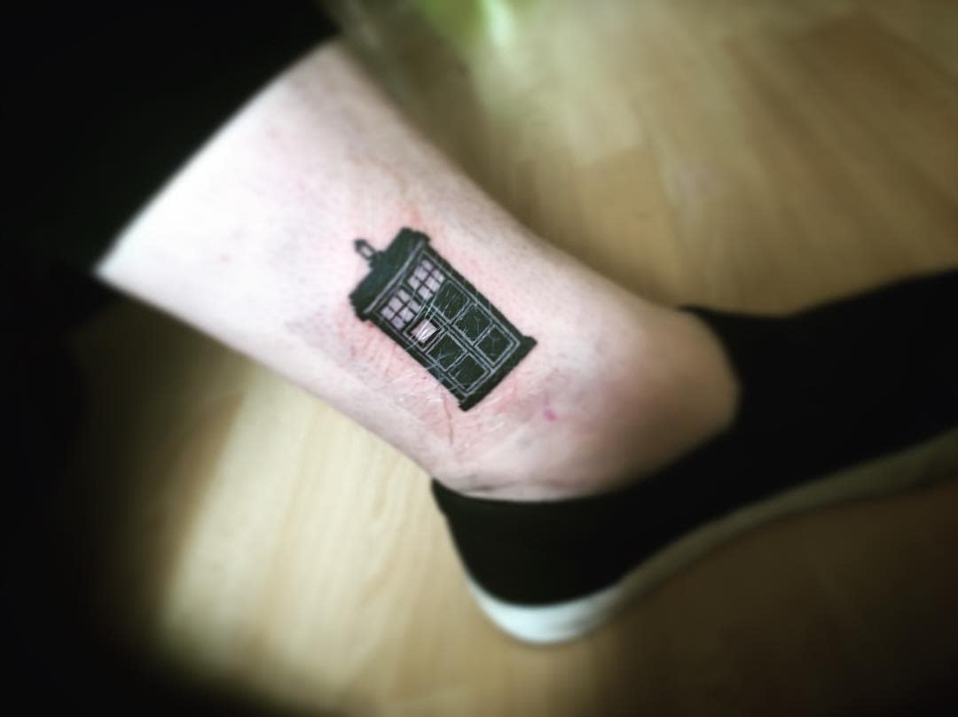 Minimalist black tattoo of the TARDIS from 'Doctor Who', executed with precise line work to capture the iconic police box design