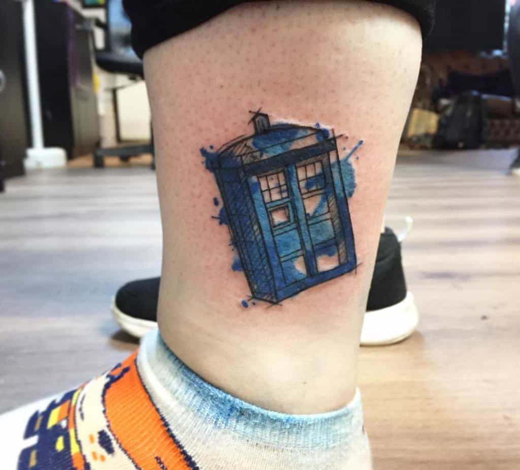 Doctor Who-inspired tattoo depicting the TARDIS with a sketchy, blue watercolor effect, splatters around the edges
