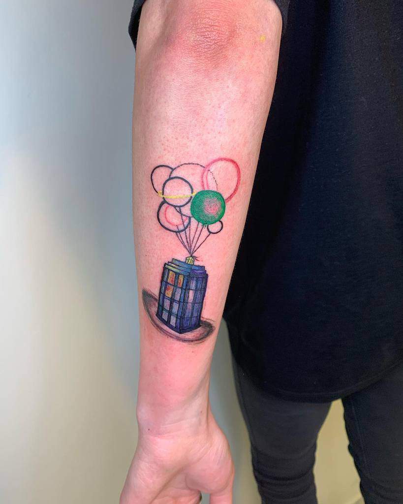 Creative Doctor Who tattoo on an arm, featuring the TARDIS lifted by a cluster of colorful balloons with string details