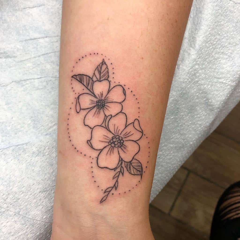 A black line floral tattoo featuring delicate dogwood flowers and leaves gracefully adorns the arm