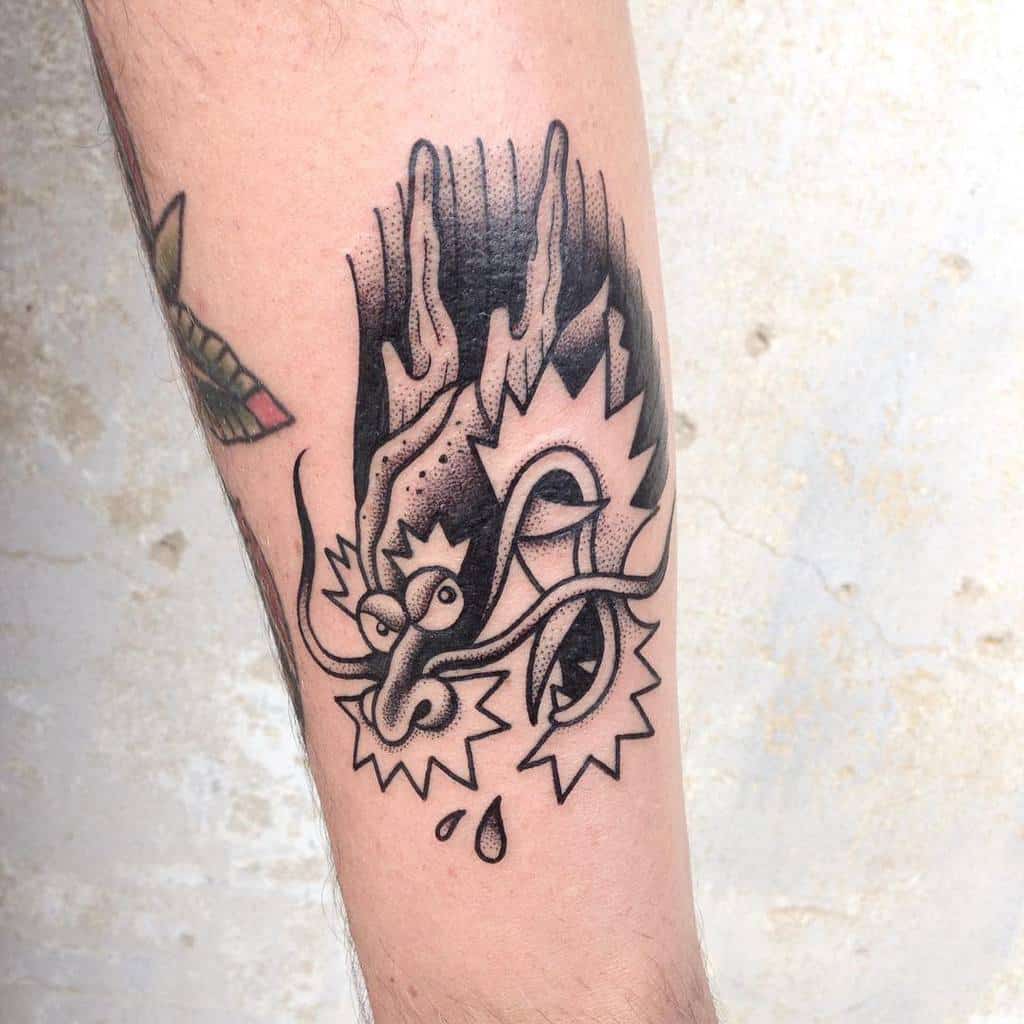 Tattoo of a stylized dragon face with flames and a tear drop on a forearm