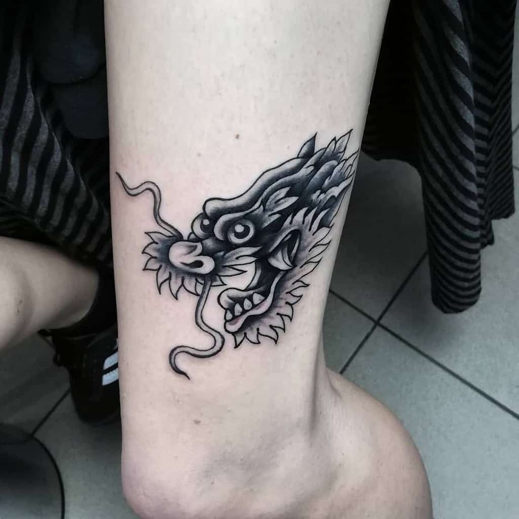 Tattoo of a dragon's head with an open mouth on a person's leg