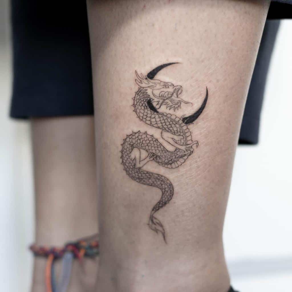 A tattoo of a dragon wrapped around a crescent moon on a woman's calf