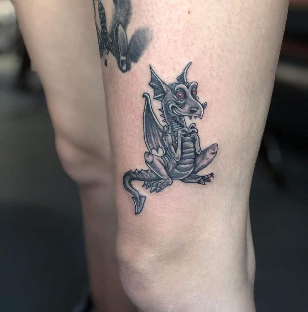 A leg tattoo of a small, cute dragon sitting with its wings folded