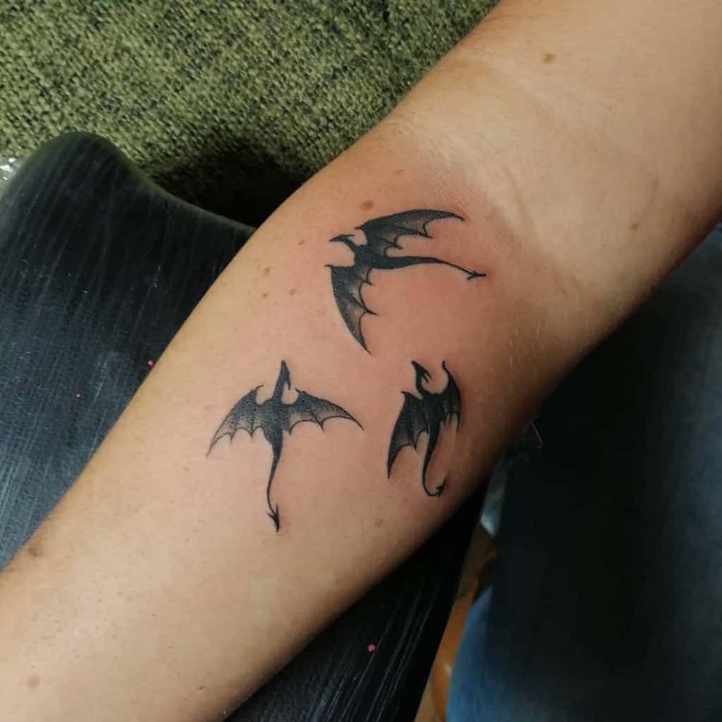 Tattoo of three black dragon silhouettes on a woman's forearm