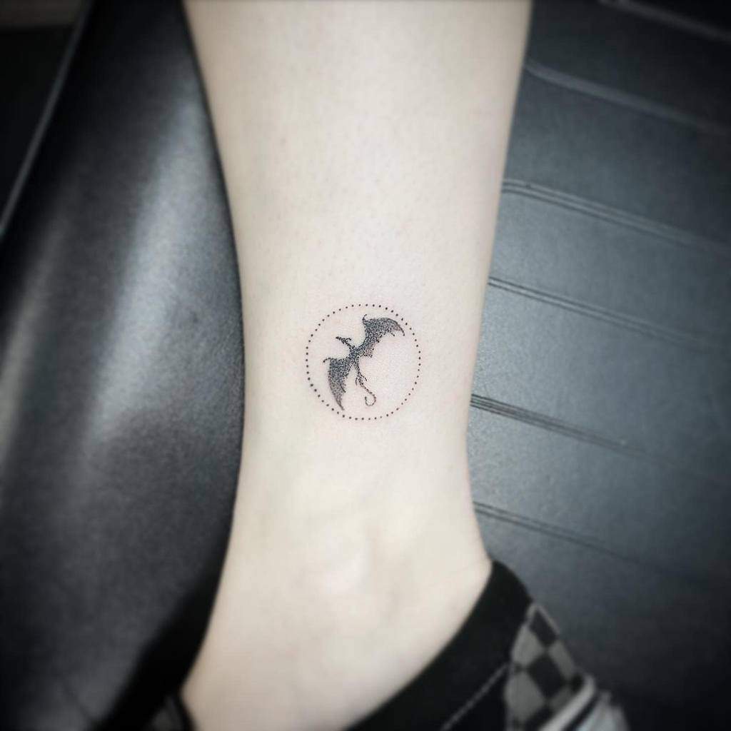 Small dragon tattoo on a forearm inside a dotted circle