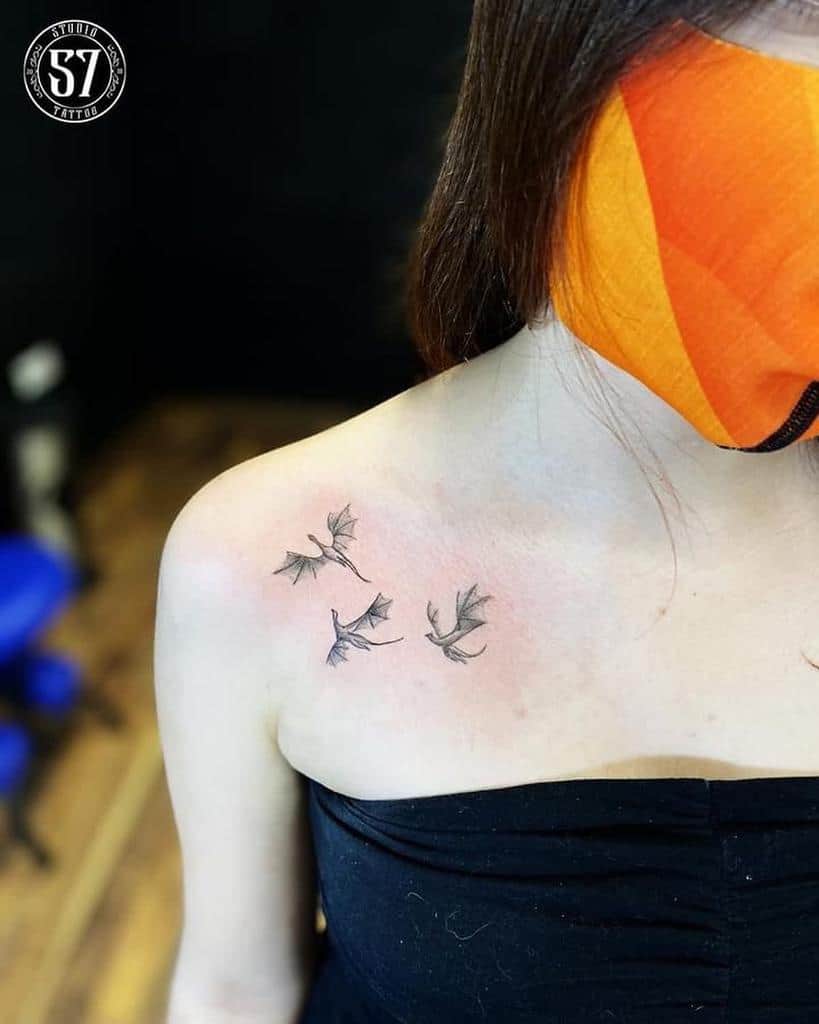 Three small bat tattoos on a woman's shoulder near the collarbone