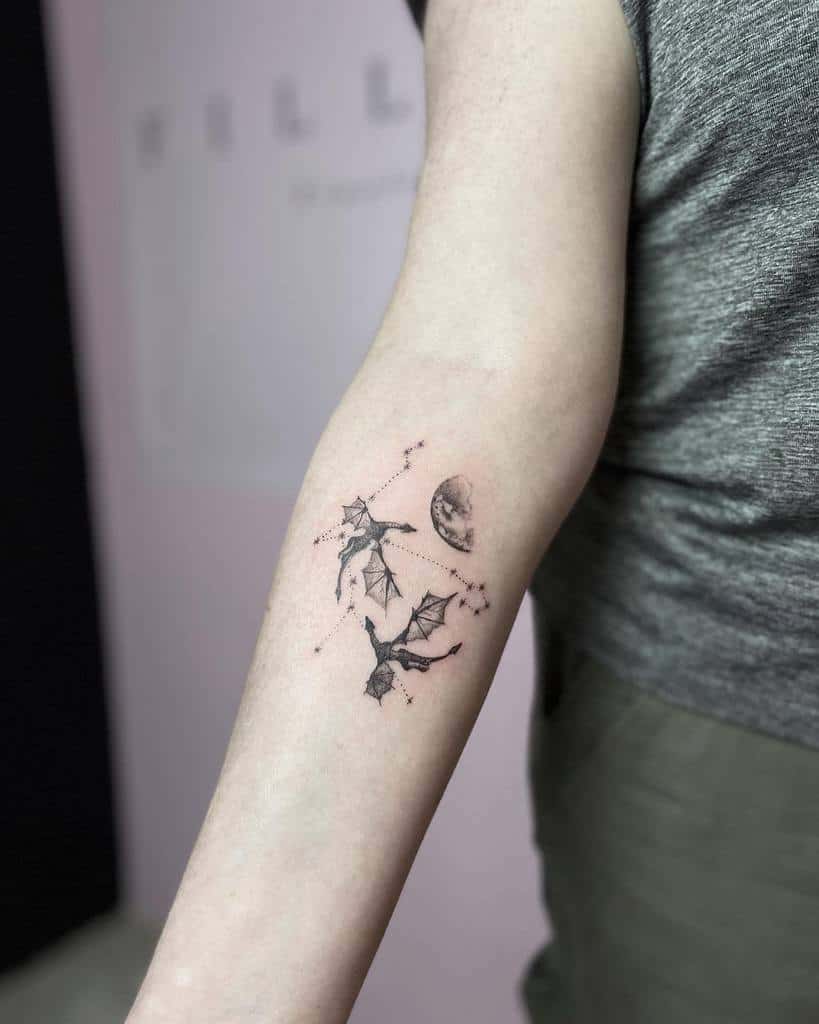 Arm with a tattoo of two dragons flying near a moon and constellations