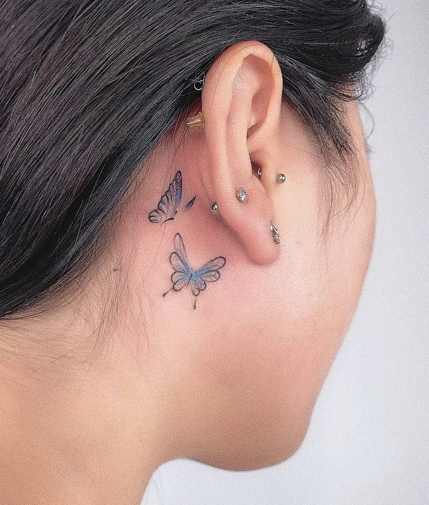 Delicate blue butterfly tattoo behind the ear, symbolizing transformation and freedom, with fine details for a soft and elegant look