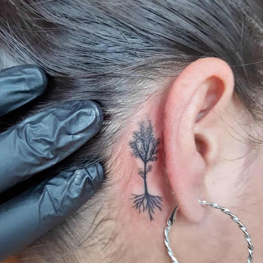 Black tree tattoo with roots behind a woman's ear