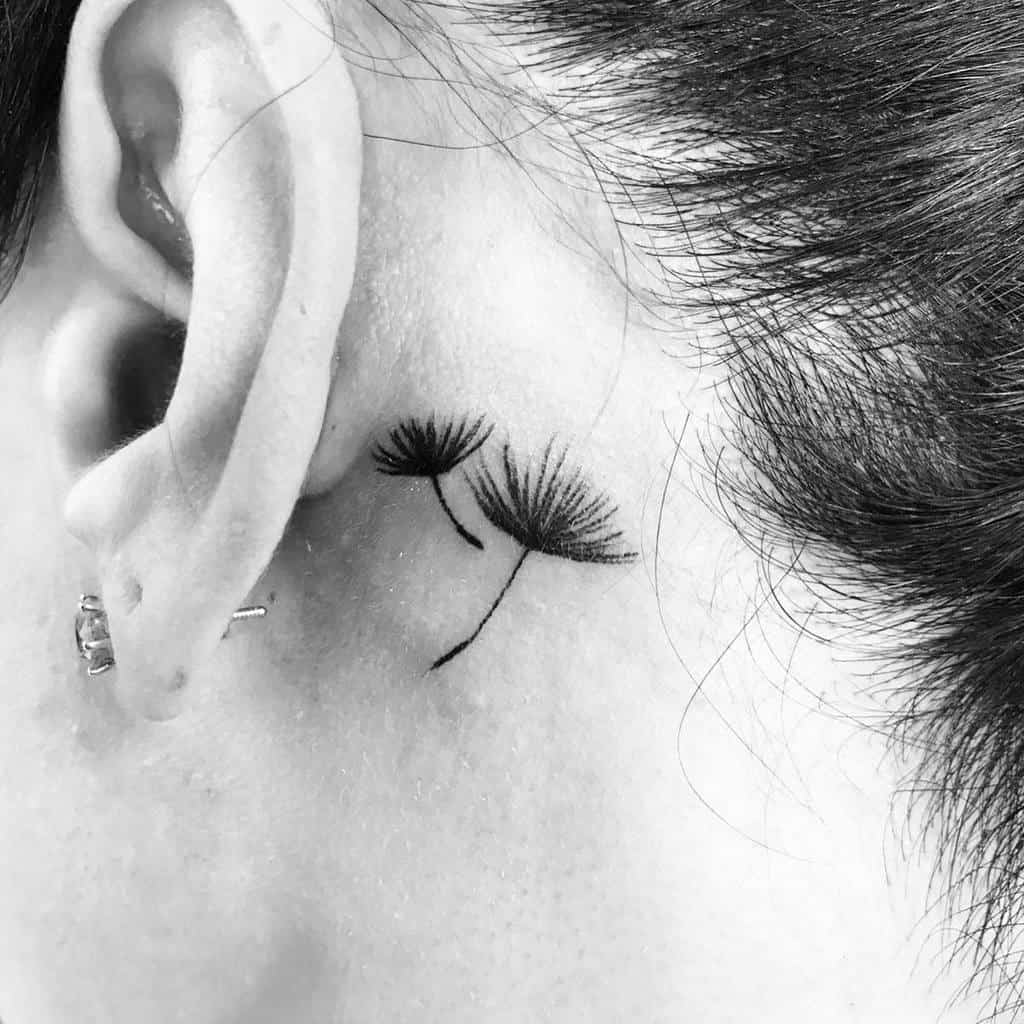 Close-up of a delicate dandelion tattoo behind a woman's ear