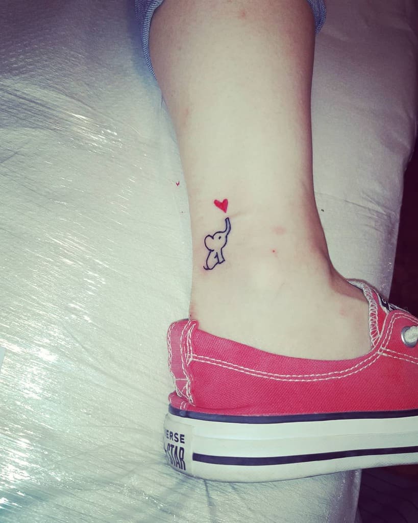 Simple elephant ankle tattoo with a red heart above the trunk, creating a playful and charming design