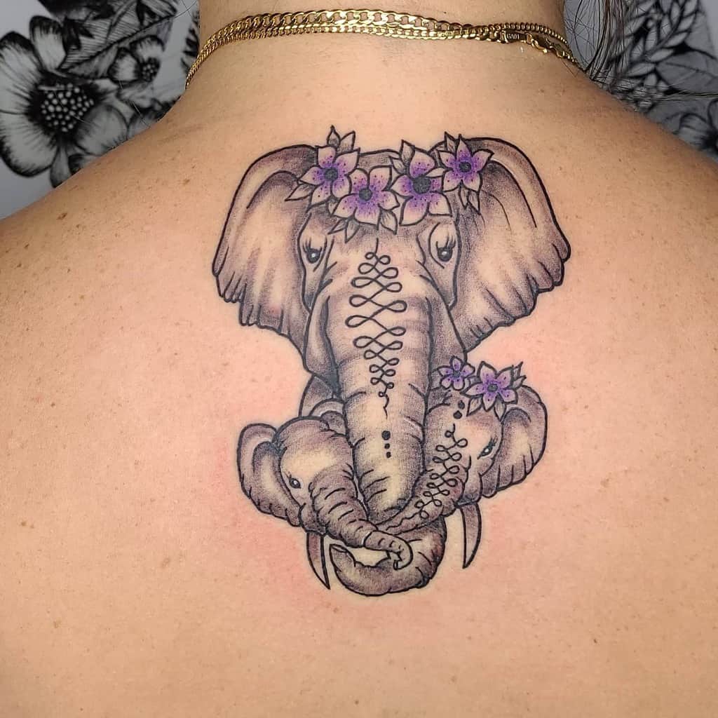 Tattoo of a mother elephant with a baby on a person's back, adorned with purple flowers